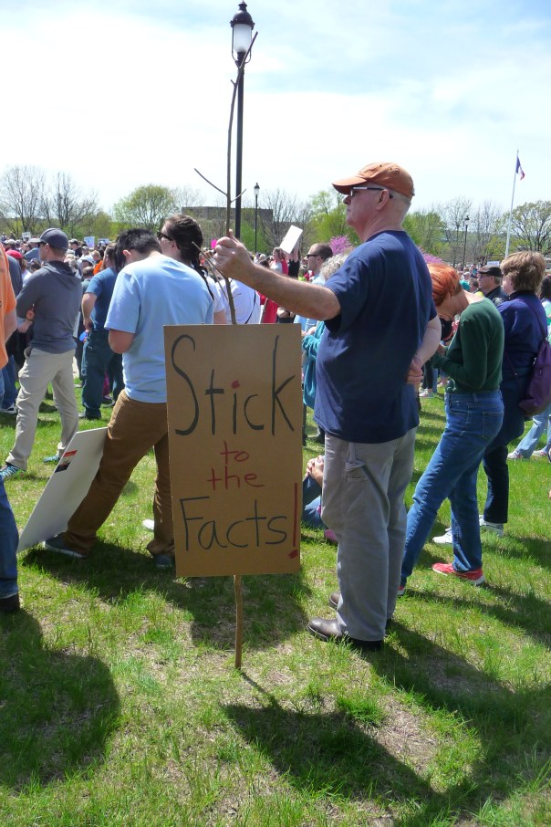 A March for Science Iowa participant holds a stick with the sign "Stick to the facts" attached to it.